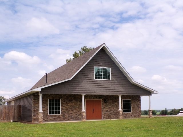 Rural house with gray roof, brick lower walls, and an orange front door under a cloudy sky
