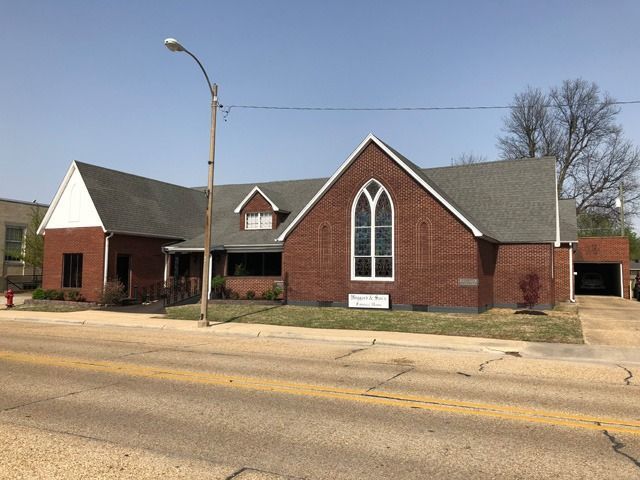 Brick church building with arched windows and a small bell tower beside a street