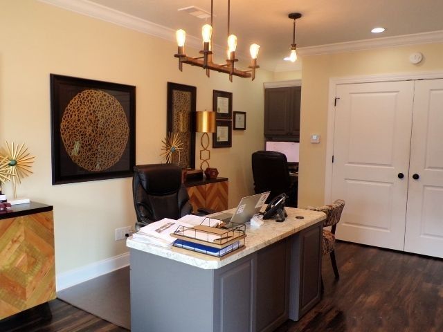 Home office with desk, chandelier, wall art, and double doors on hardwood floor.