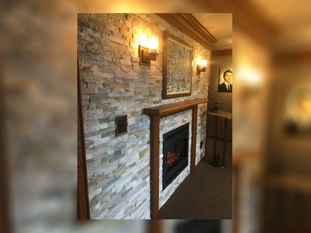 Stone fireplace with wall sconce and framed art in a cozy interior hallway