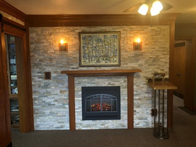 Living room fireplace with stone surround, wood trim, wall sconces, and framed artwork above the mantel