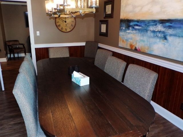 Dining room with long wooden table, upholstered chairs, chandelier, and abstract wall art.
