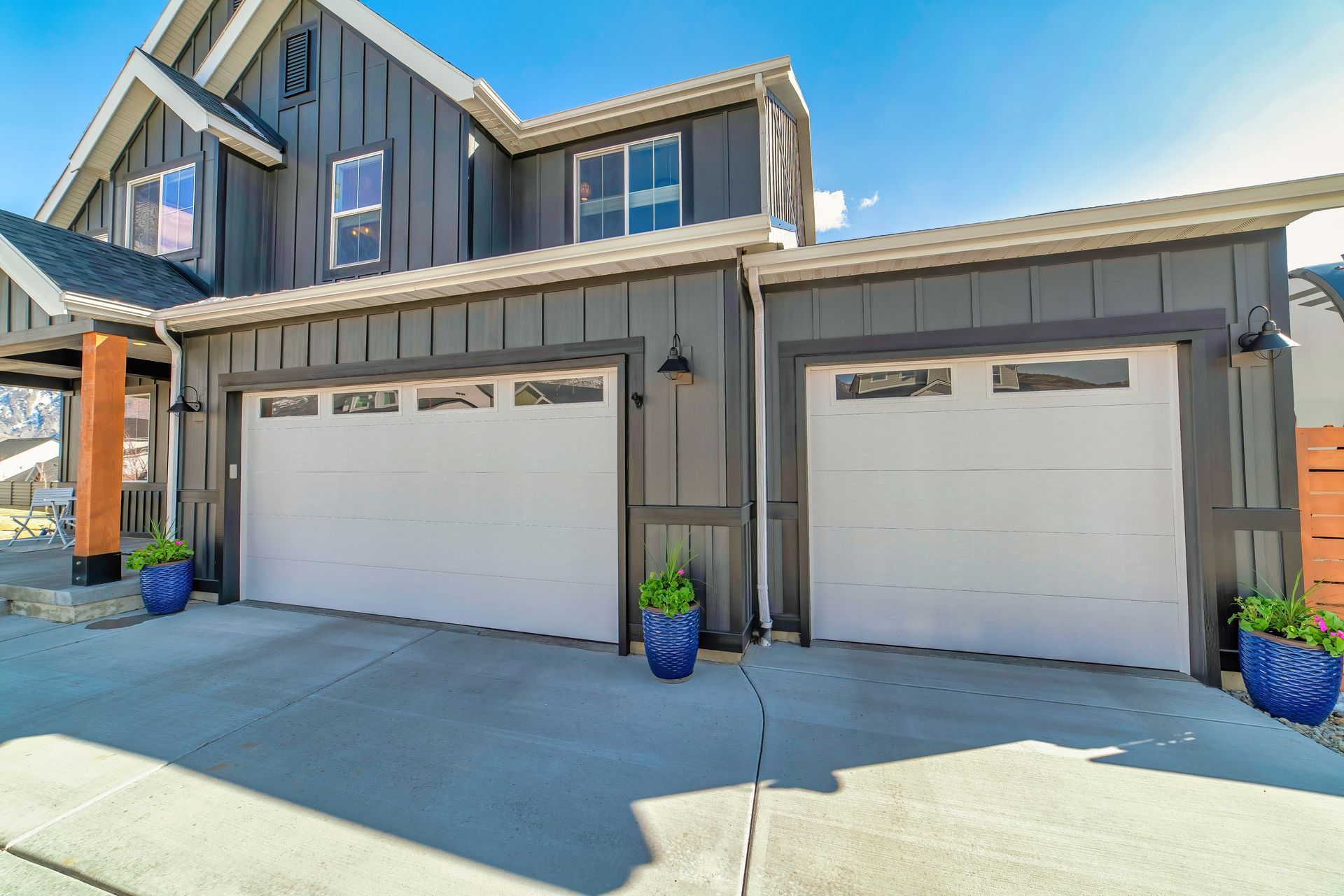 Modern two-story house exterior with two white garage doors and blue flower pots on the driveway