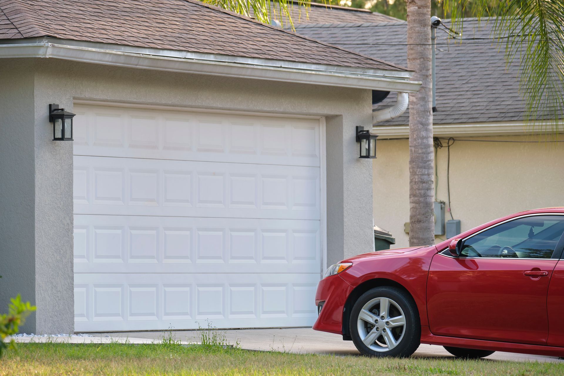 Red car parked in front of a white garage door in a suburban home driveway.