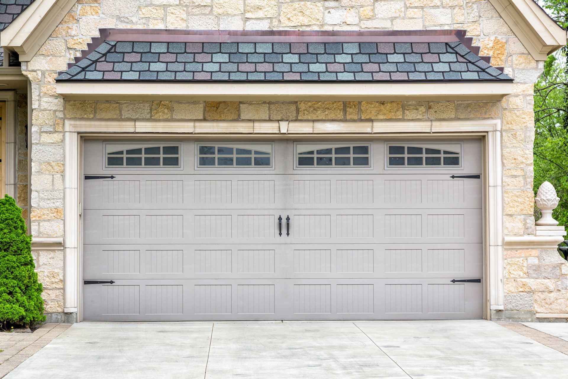 Two-car beige garage with gray doors and stone house facade