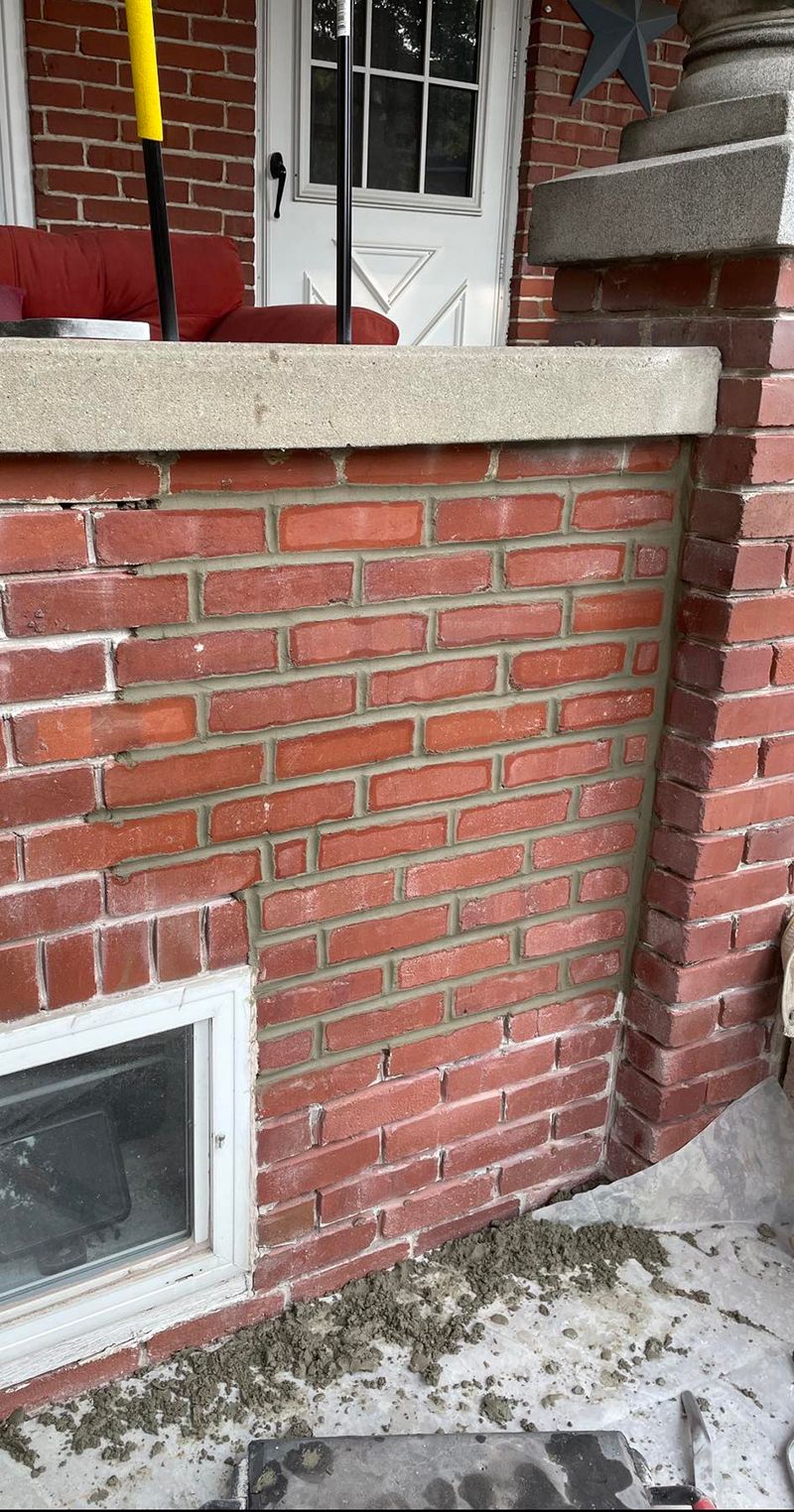 Red brick wall with new mortar; small basement window; building exterior.