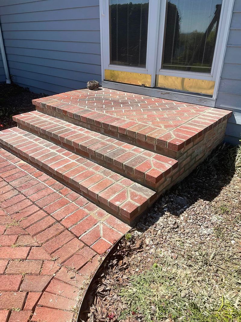 Brick steps leading up to a doorway; brick pathway curves in front of steps; green grass on the right.