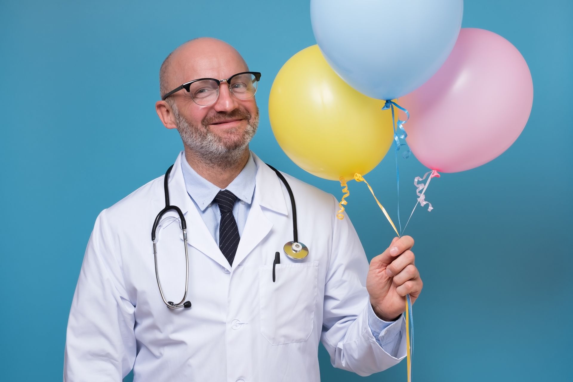 Médico comemorando o natal Médico sorrindo enquanto segura balões coloridos contra um fundo azul.