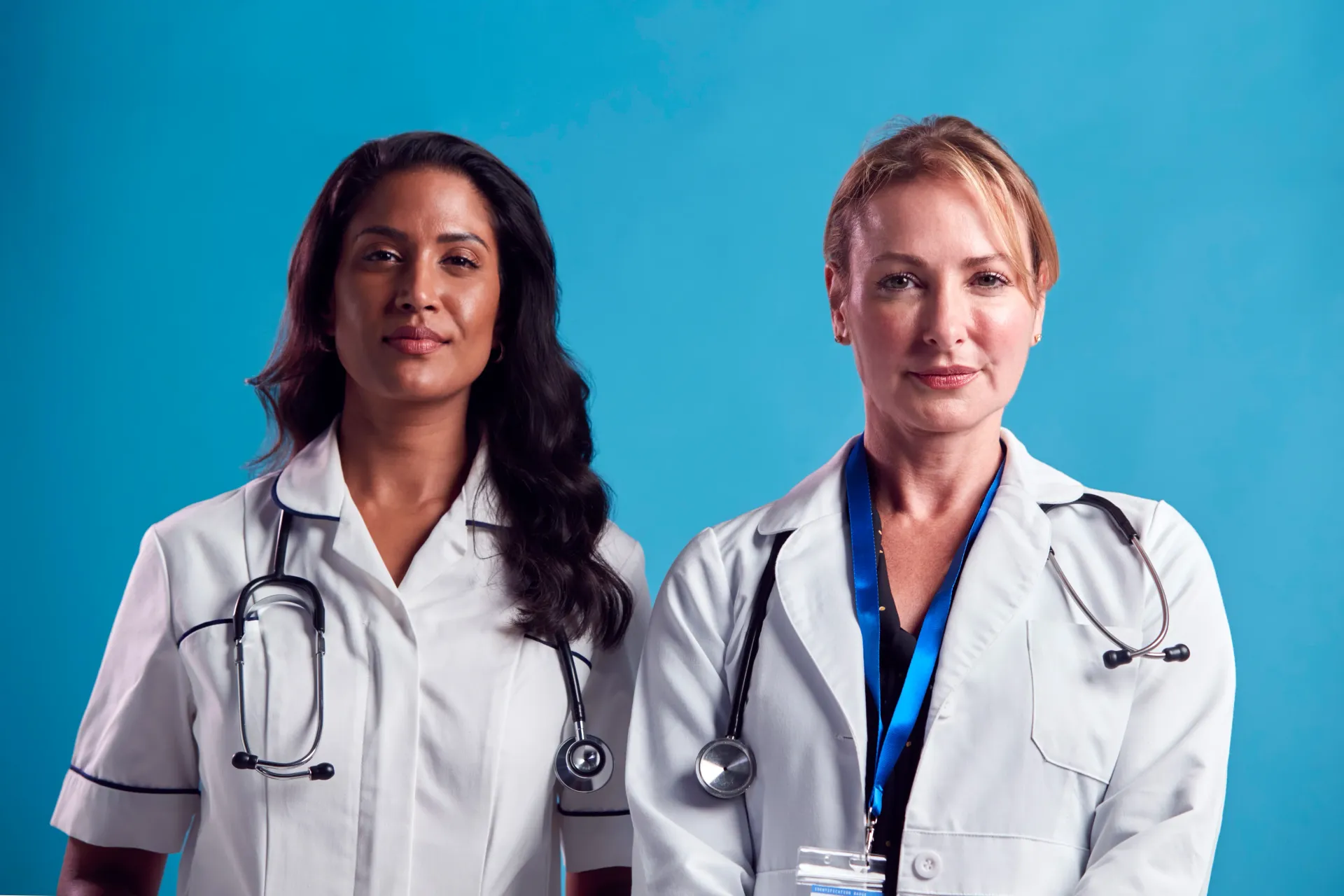 Dois profissionais da área médica com estetoscópios contra um fundo azul.