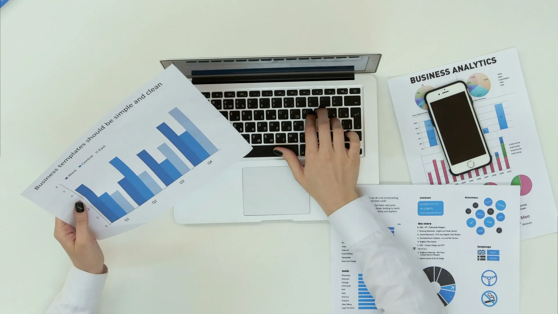 Pessoa digitando em um laptop, analisando gráficos em azul e branco e usando um smartphone.