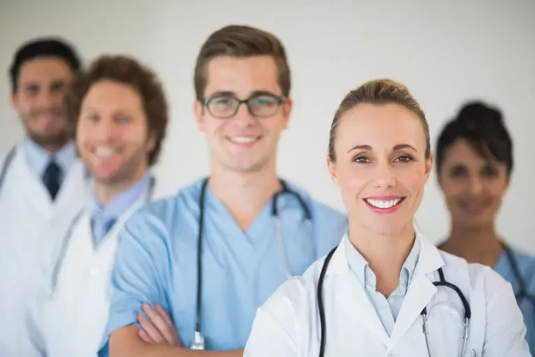 Equipe médica utilizando software seguro com controle de acesso personalizado. Equipe médica sorridente, vestindo uniformes cirúrgicos e jalecos brancos, com estetoscópio, em um ambiente bem iluminado.