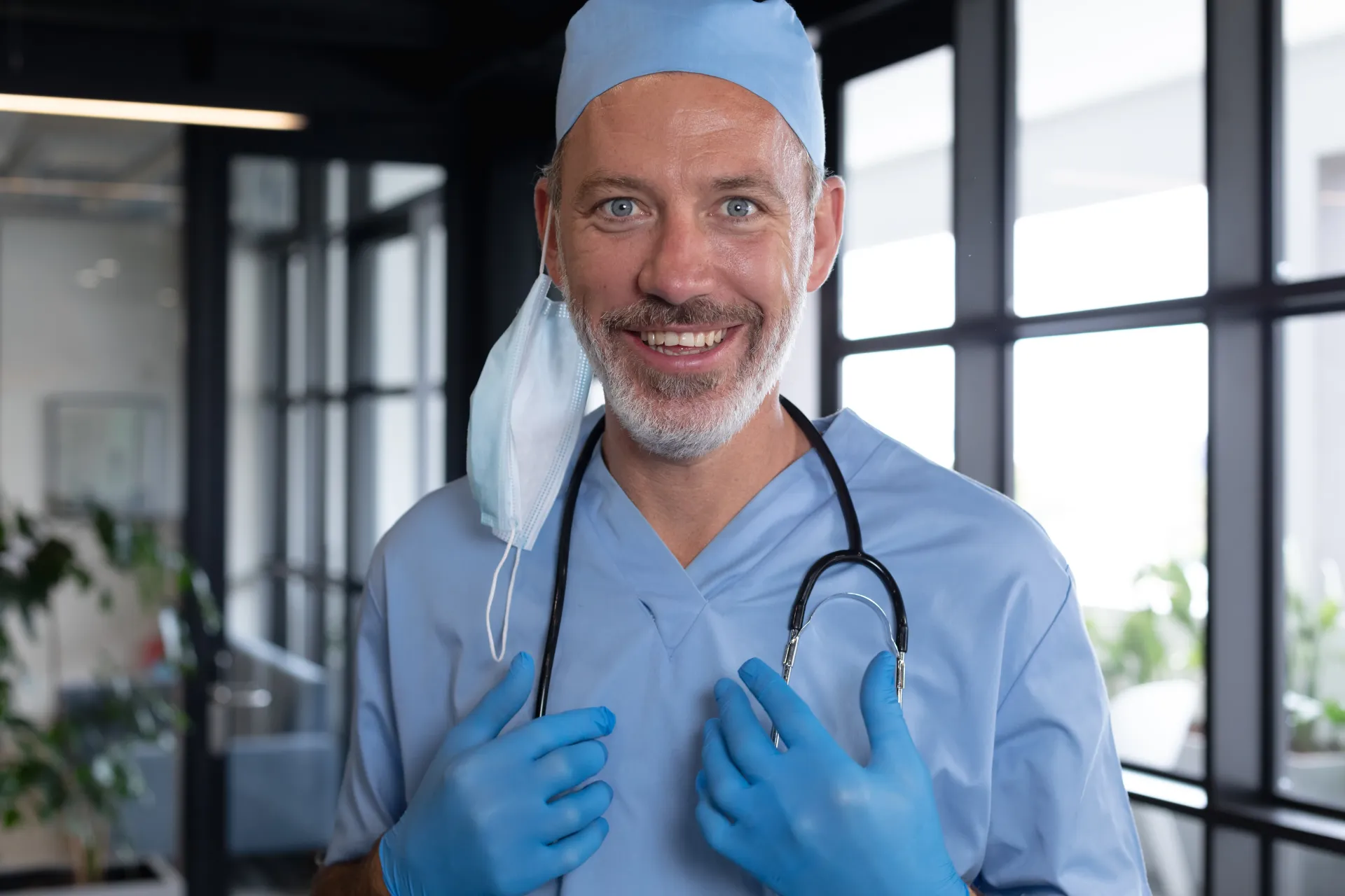 Profissional de saúde de uniforme azul, sorrindo, com estetoscópio e máscara no pescoço.