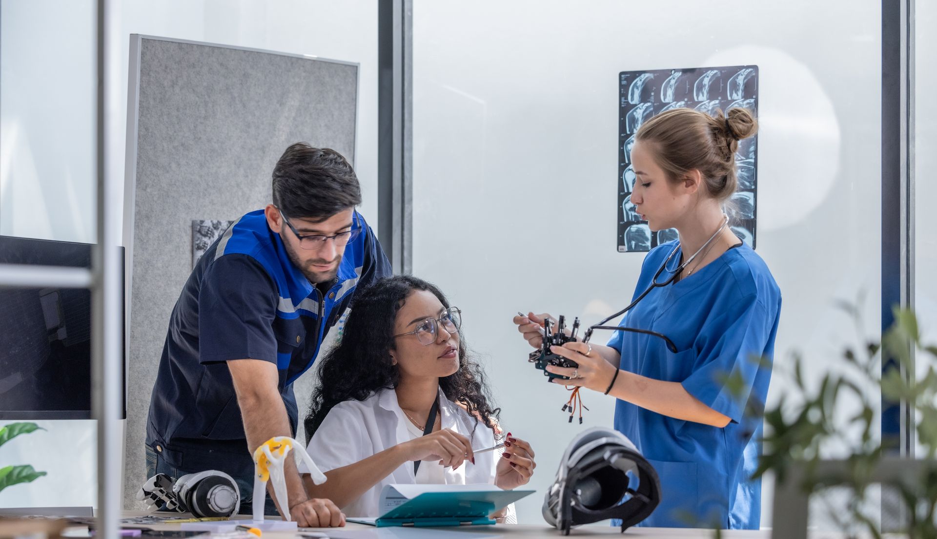 Três profissionais da área médica conversando, um deles segurando um objeto, em um consultório moderno com imagens médicas.