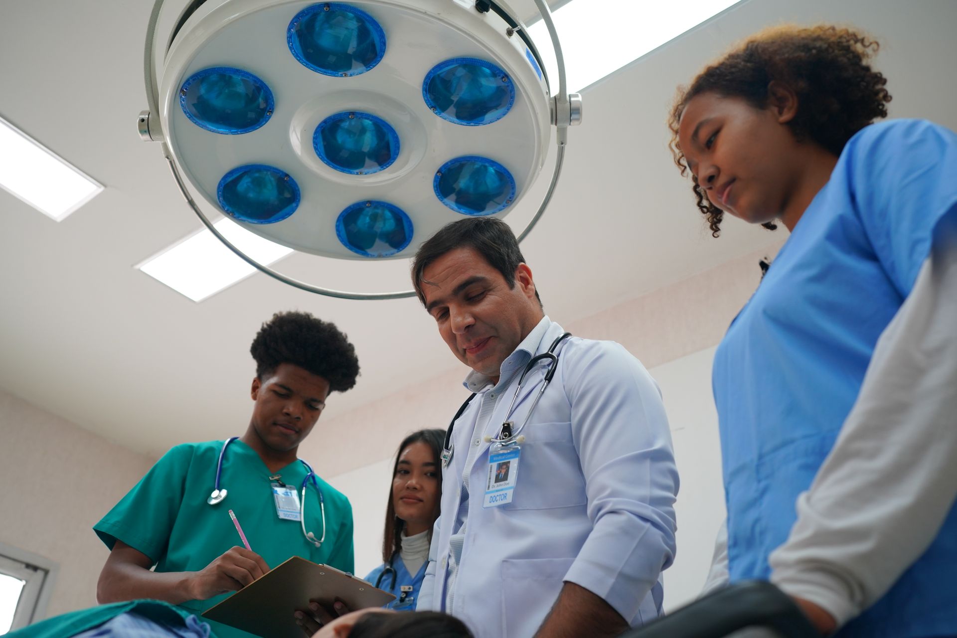 Equipe médica na sala de cirurgia, examinando o paciente. Luzes fortes no teto.