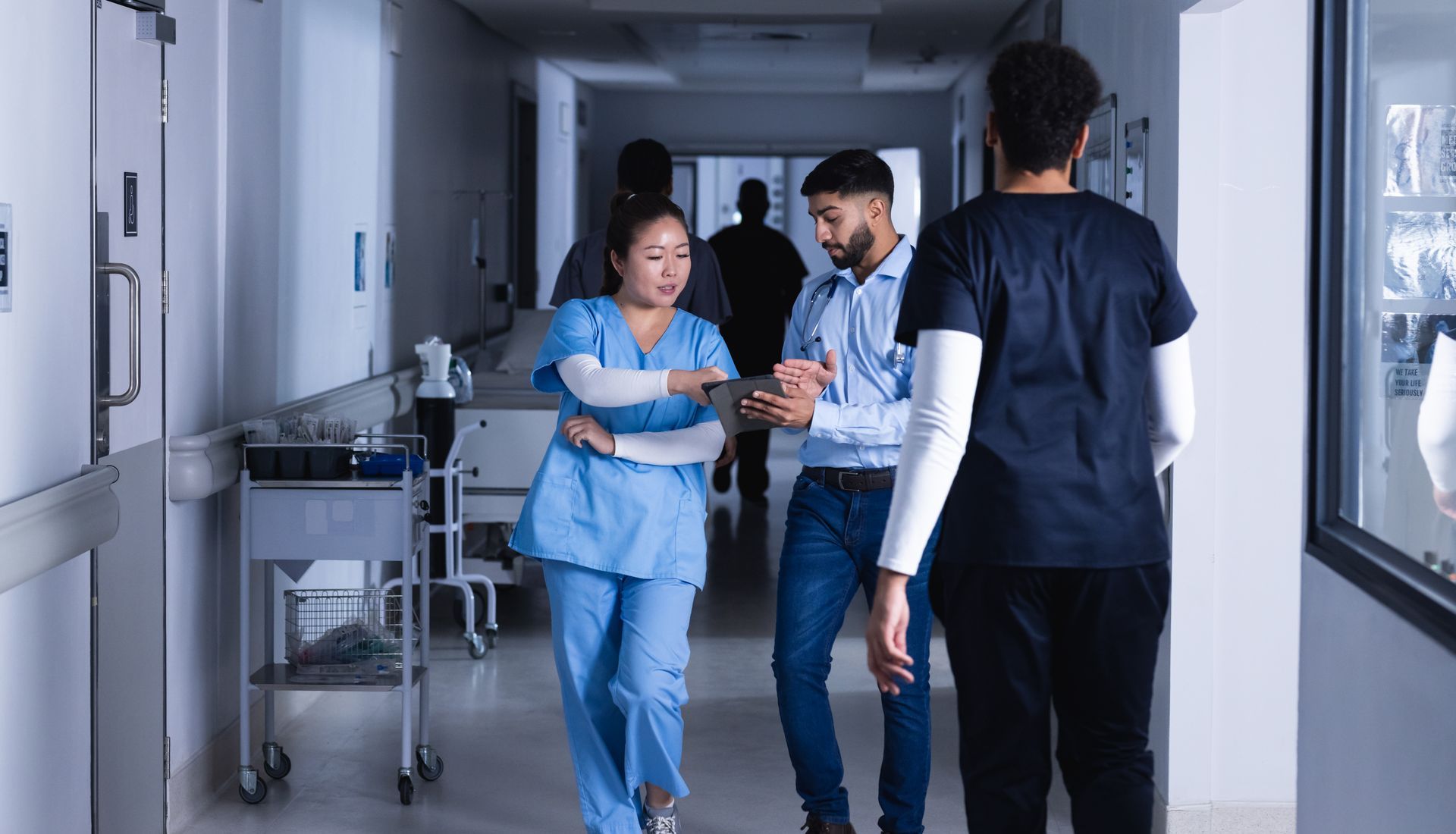 Fast Track na Medicina em 2025 Corredor do hospital com profissionais de saúde conversando; um de uniforme médico, dois com roupas casuais, um de uniforme médico olhando para o lado.