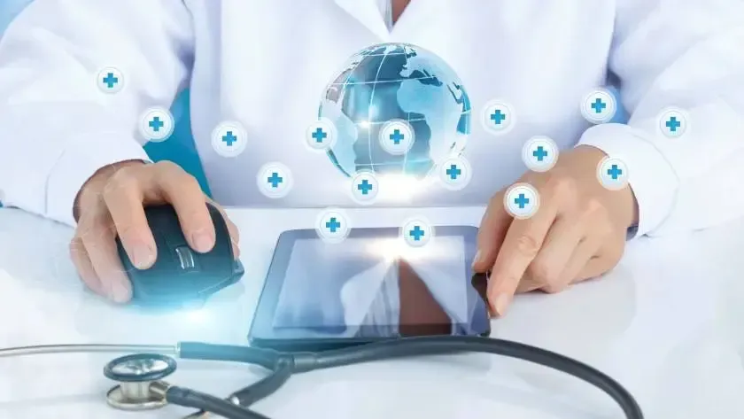 Médico usando tablet e mouse, com um globo terrestre e símbolos médicos flutuando acima, estetoscópio em primeiro plano.