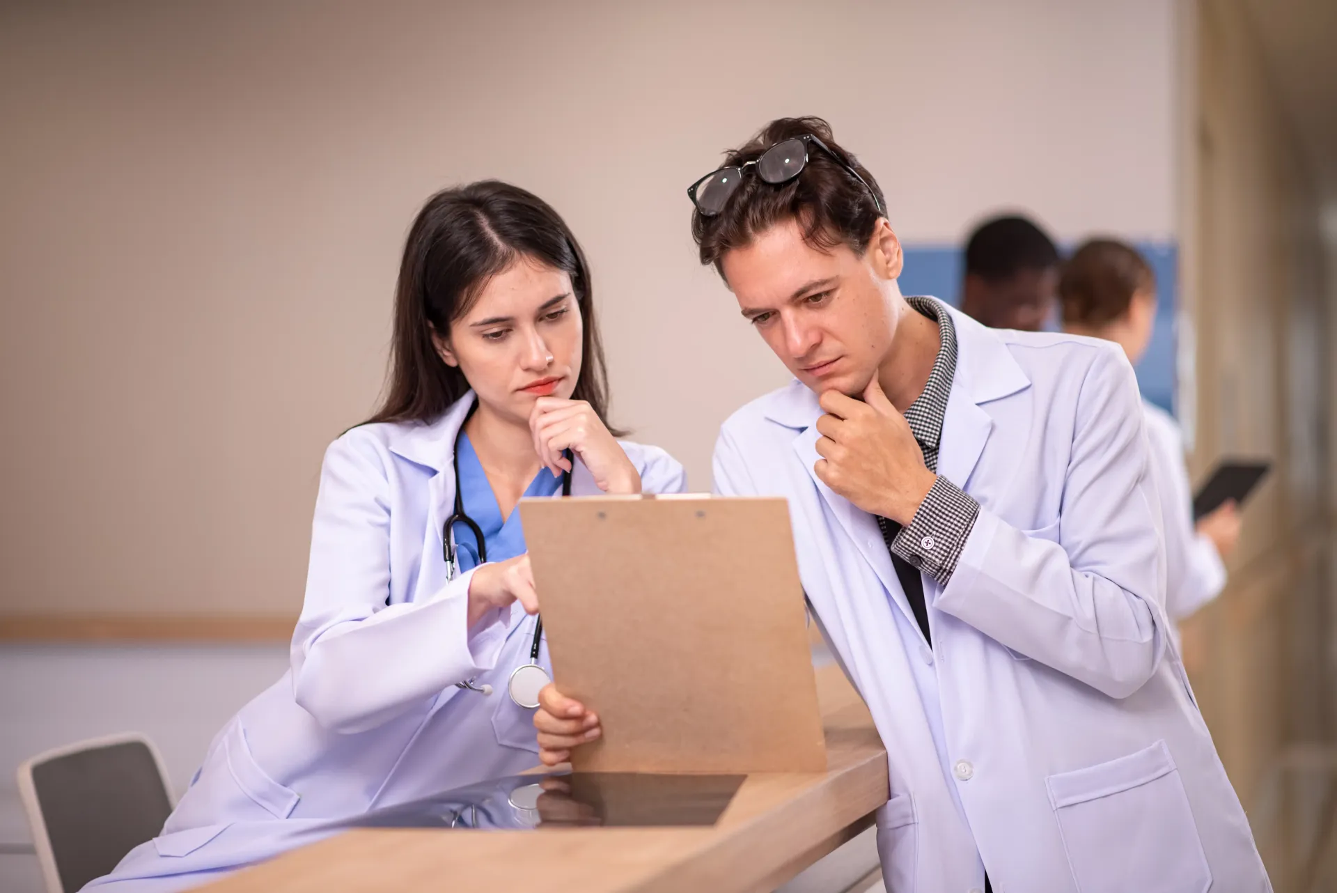 Acompanhe e gerencie orçamentos de forma automatizada. Dois médicos de jaleco branco examinam uma prancheta, com semblante preocupado, em um ambiente hospitalar.