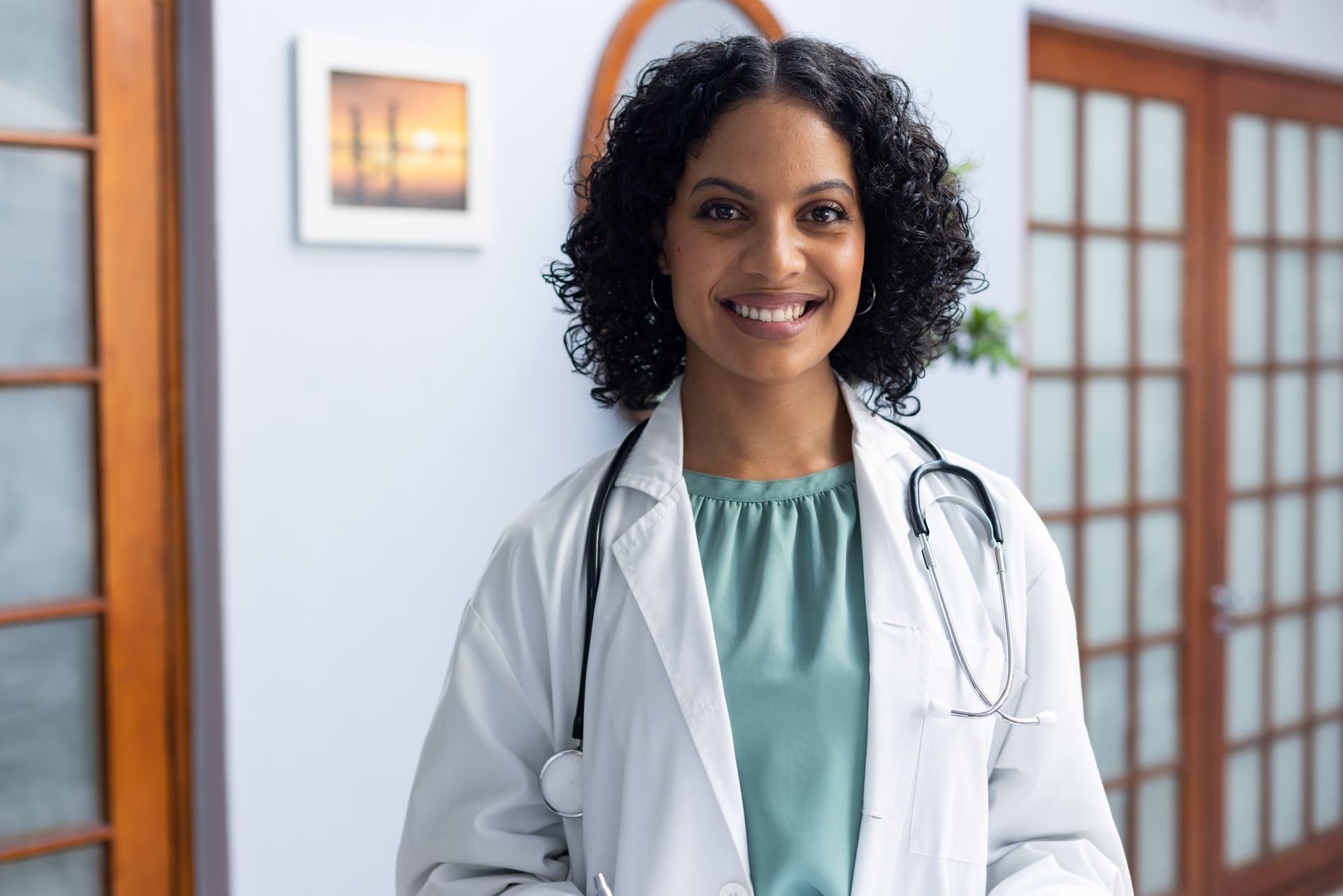 Médico de jaleco branco e estetoscópio sorri para a câmera.