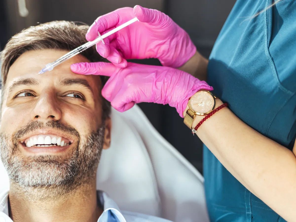 Profissional aplicando preenchedores faciais em um paciente. Homem recebendo uma injeção estética na testa, aplicada por uma pessoa usando luvas cor-de-rosa.