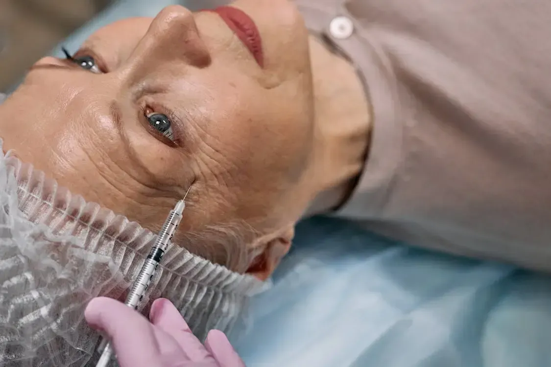 Ação para redução de gordura localizada. Pessoa recebendo uma injeção estética perto do olho; ambiente médico.