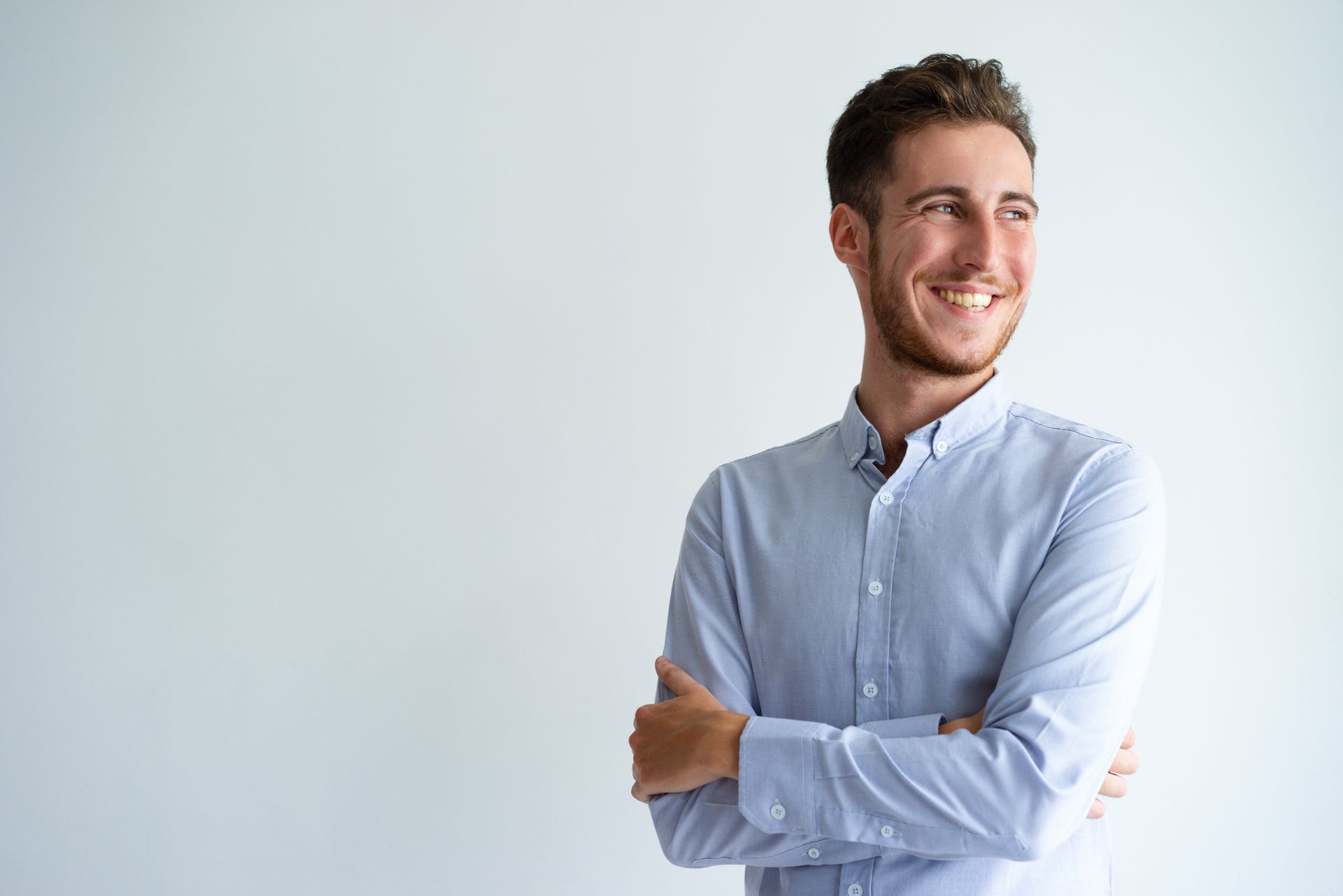 Homem de braços cruzados, sorrindo, vestindo uma camisa azul-clara de botões.