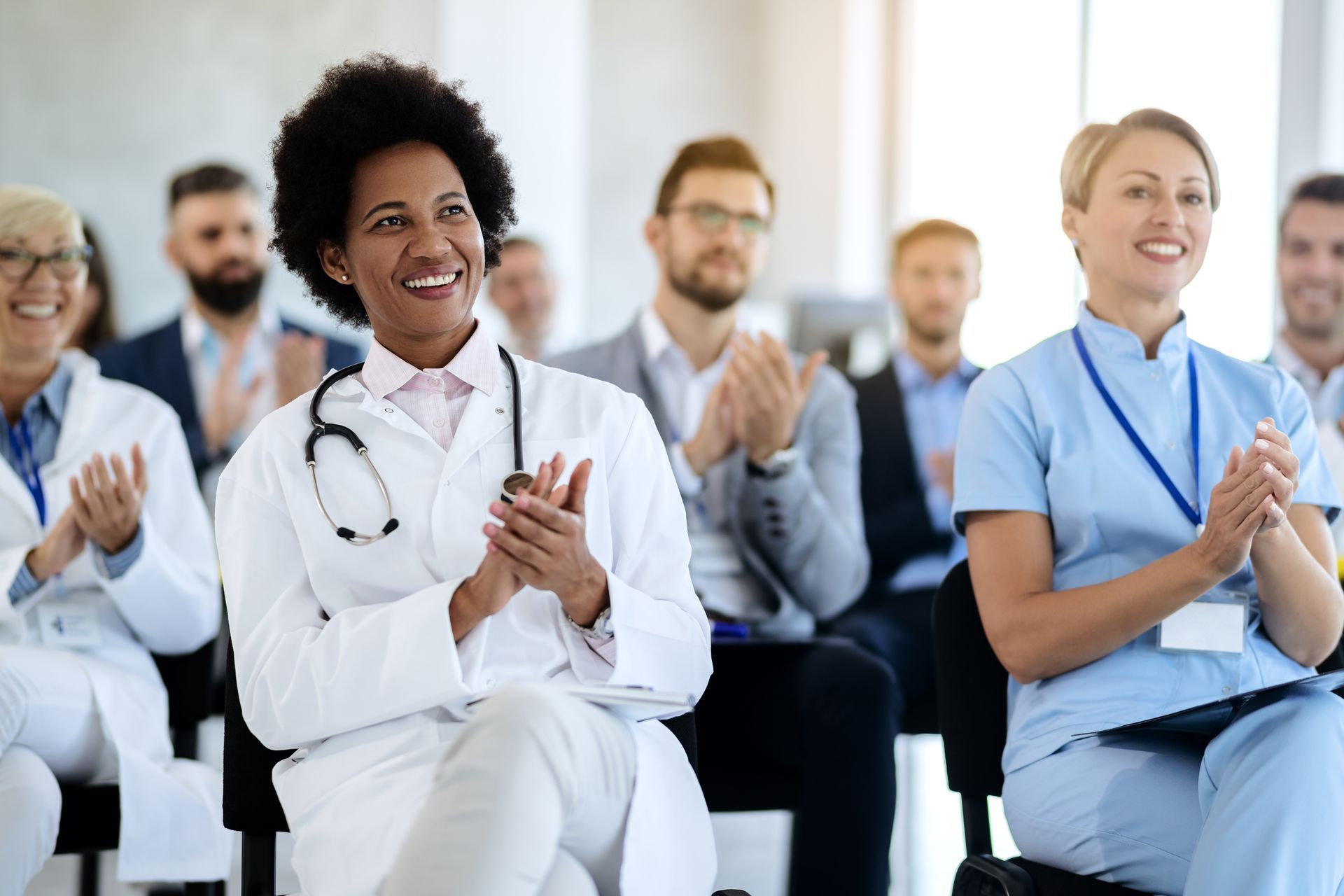 Pessoas vestidas com trajes médicos aplaudem durante uma conferência ou seminário.