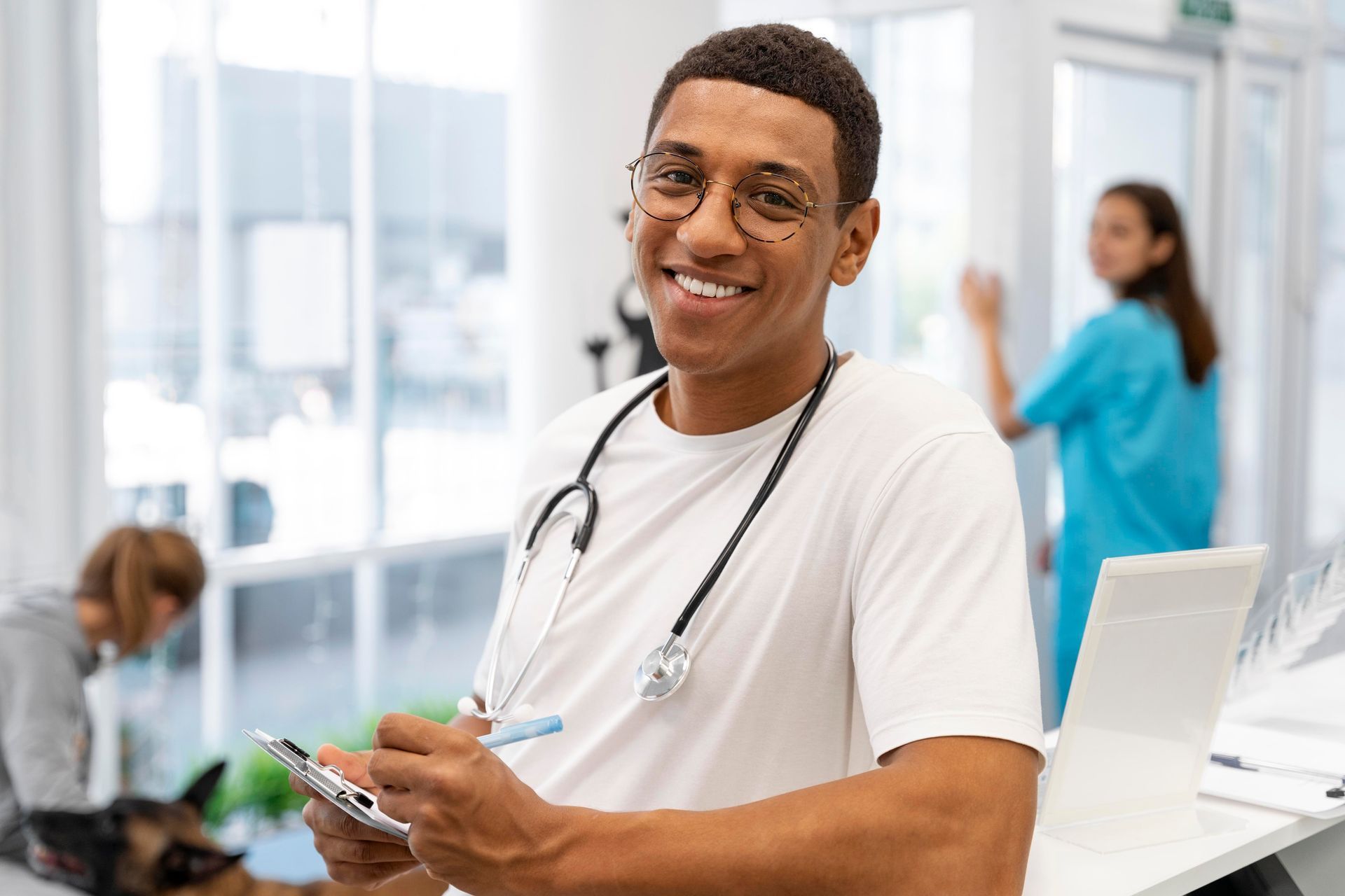 Médico com estetoscópio sorri para a câmera enquanto anota em uma prancheta em um consultório médico.