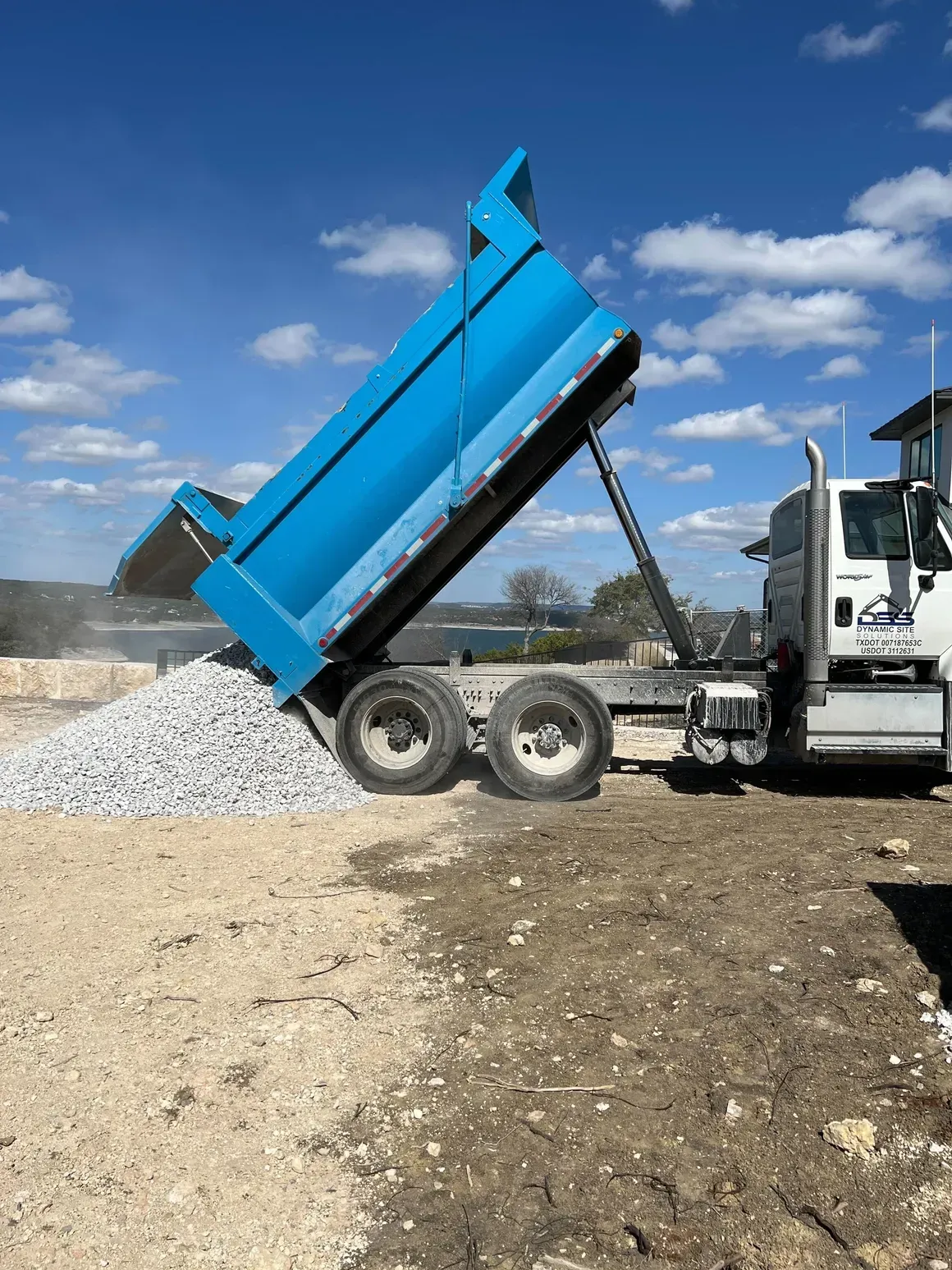 A dump truck is being loaded with gravel in a dirt field.