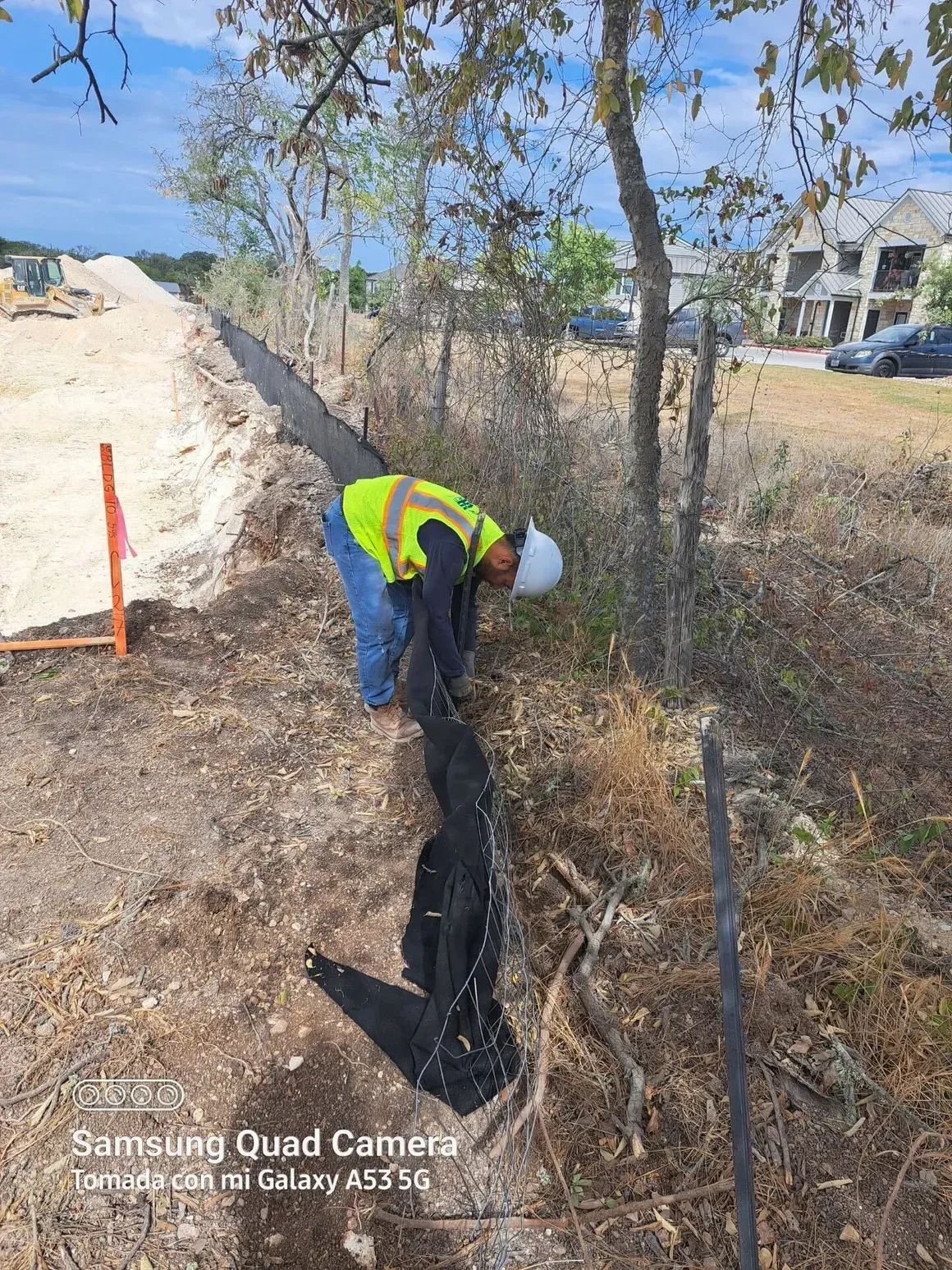 A man in a yellow vest and hard hat is working on a fence.