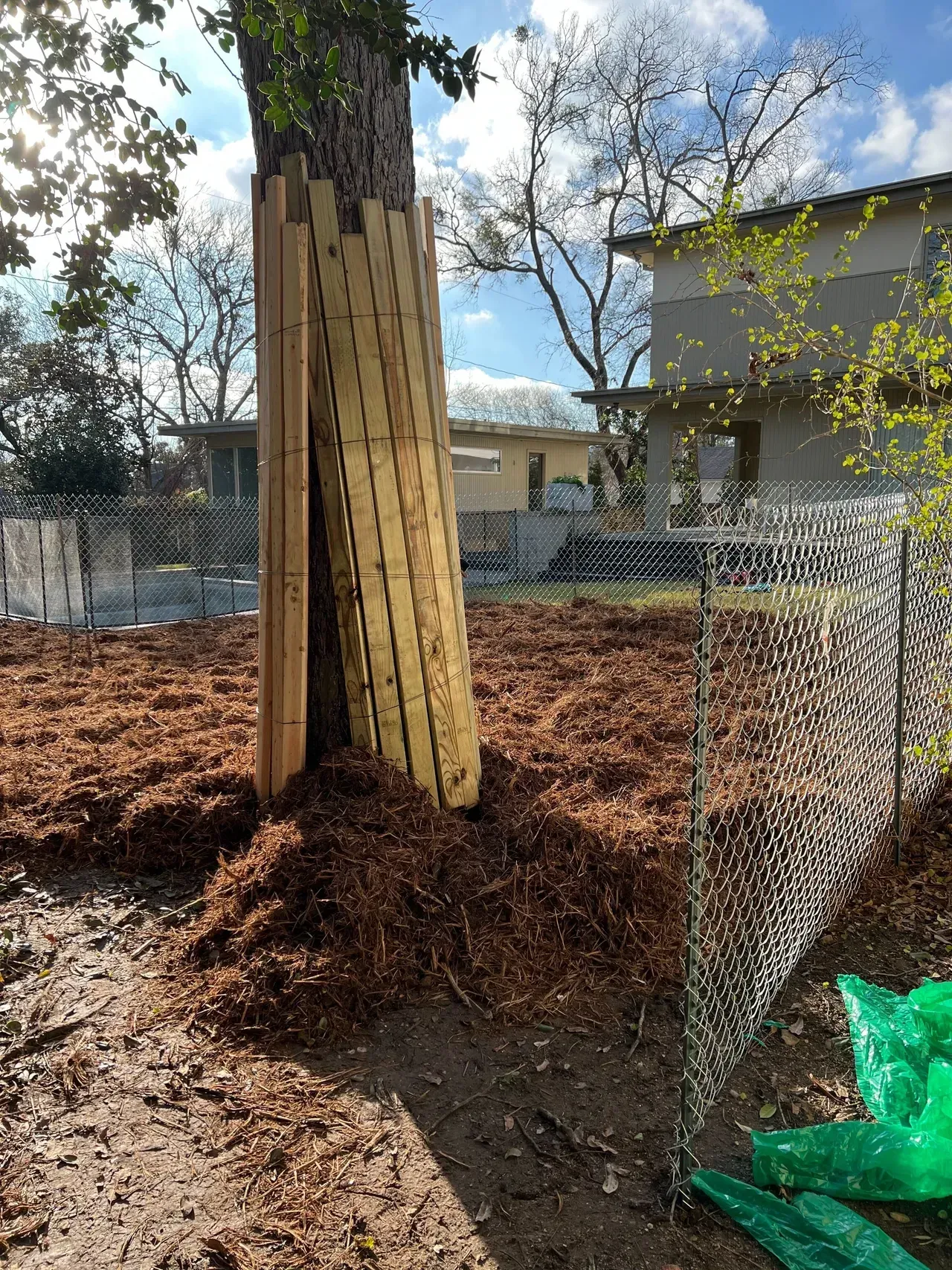 A wooden fence is being built around a tree in a yard.