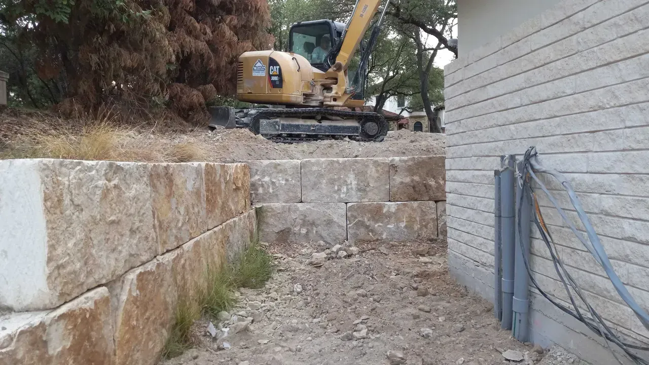 A bulldozer is working on a stone wall next to a house.