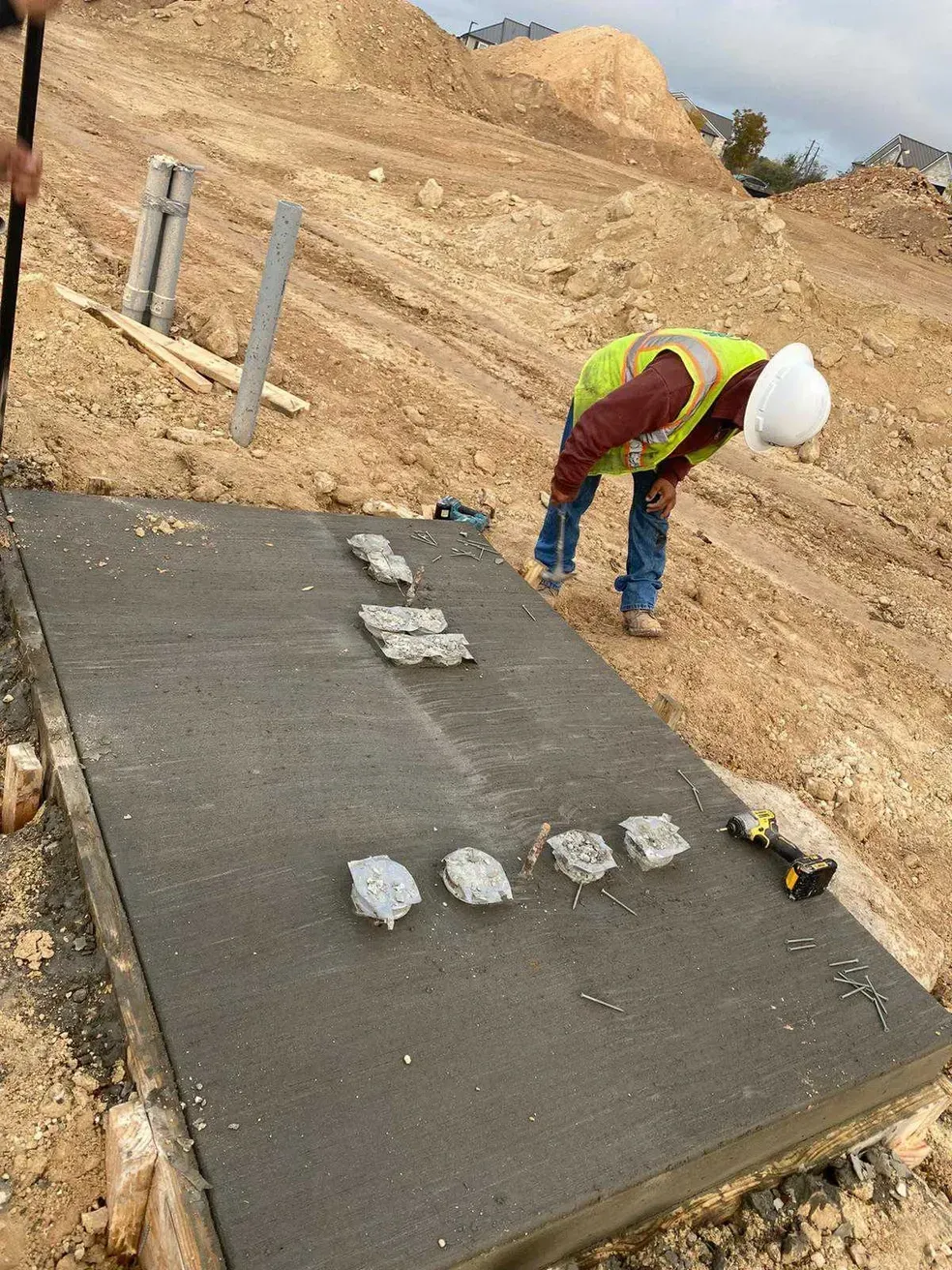 A construction worker is working on a concrete slab on a dirt road.