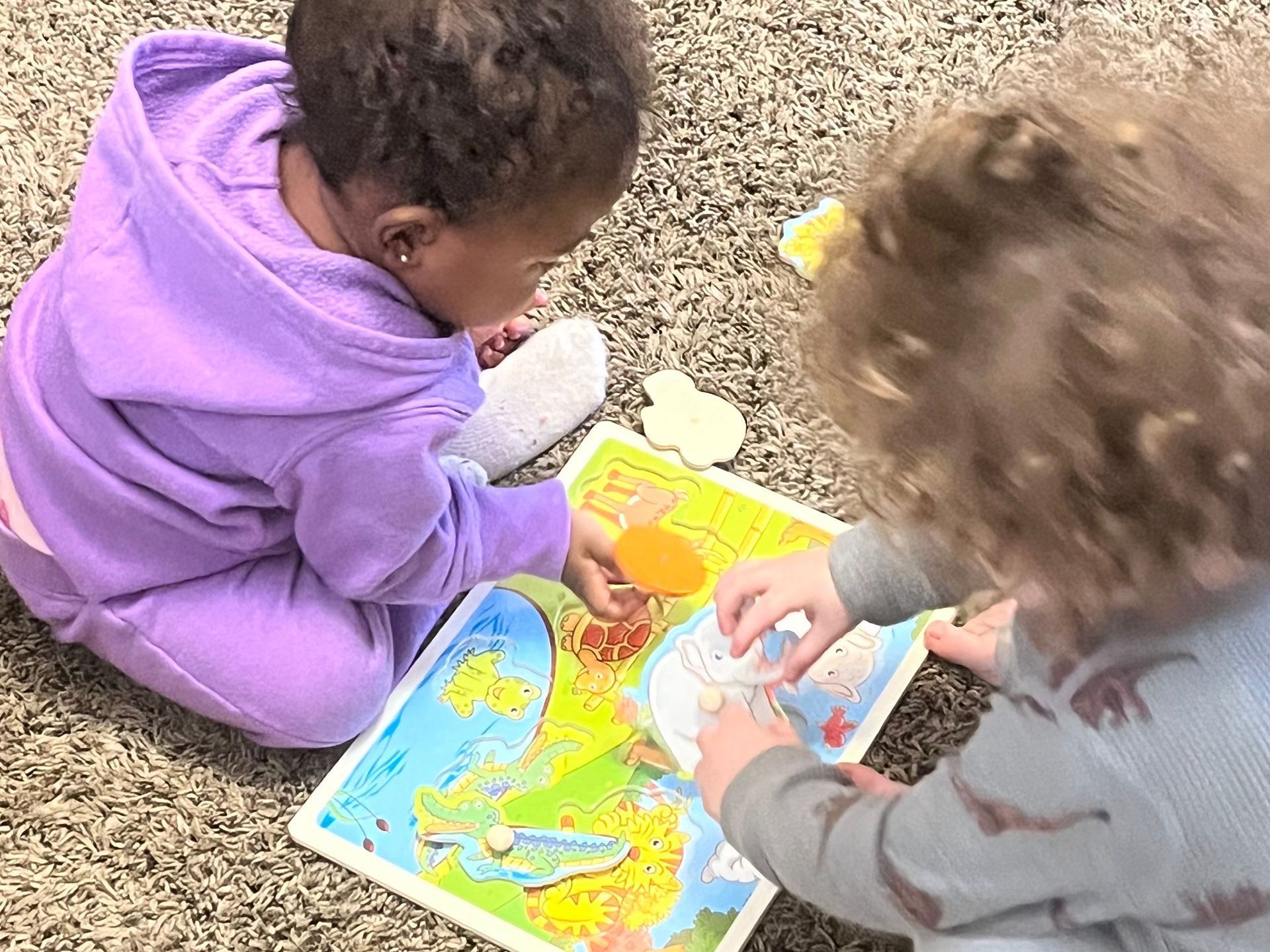 Two children are sitting on the floor playing with a puzzle.