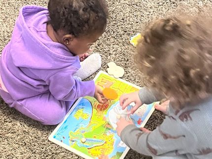 Two children are sitting on the floor playing with a puzzle.