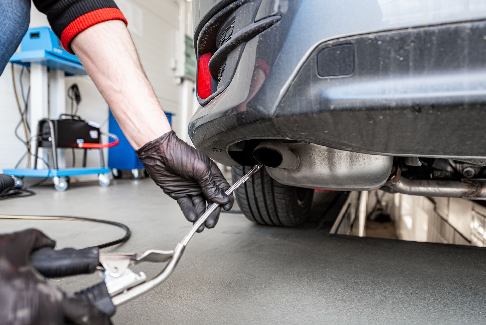 Person in black gloves testing car emissions with a probe at the exhaust pipe.