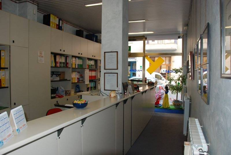 Stretto corridoio d'ufficio con banconi bianchi, scaffali e una porta luminosa in fondo.