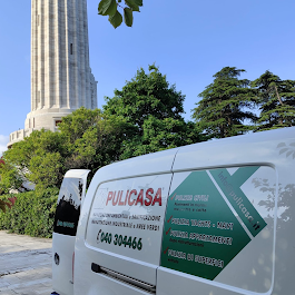 Un furgone bianco con insegne verdi parcheggiato accanto a un'alta torre di pietra e ad alberi, sotto un cielo azzurro.