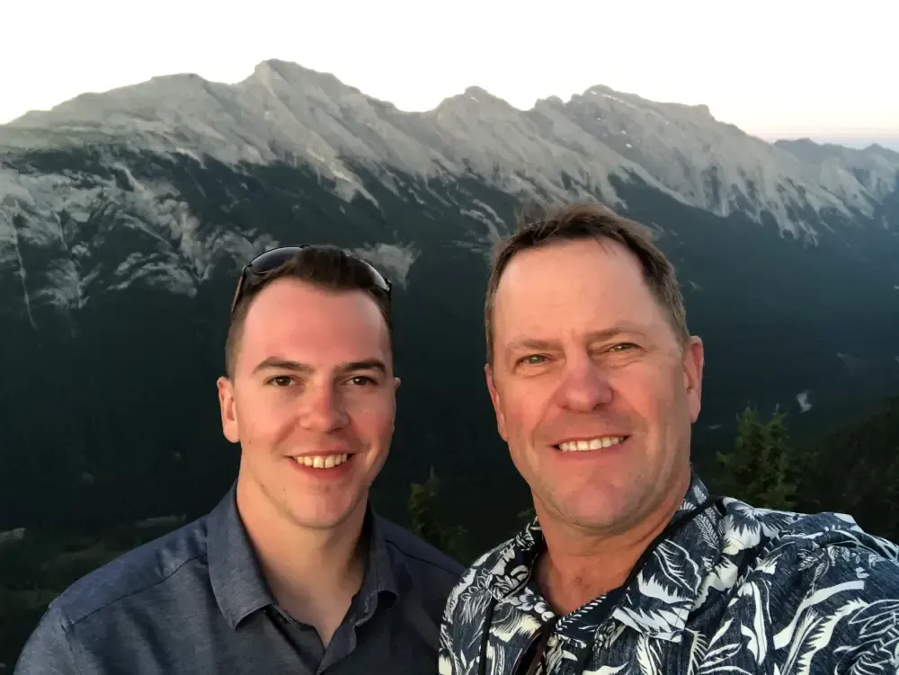 Two men are posing for a picture in front of a mountain.