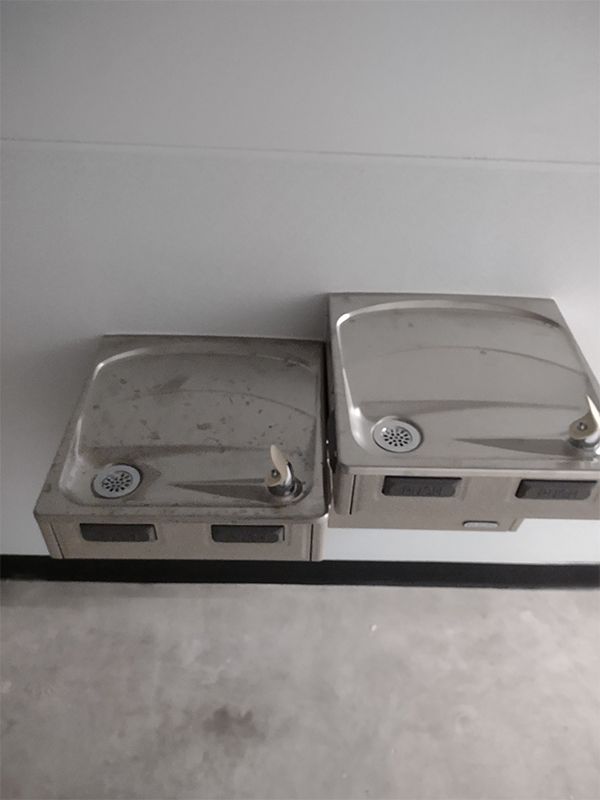 Two stainless steel water fountains are sitting next to each other on a wall.