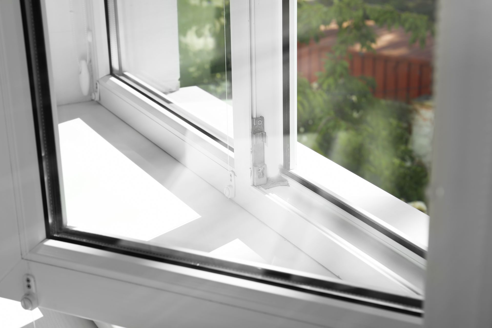 White window partially open, letting sunlight onto the sill with a view of greenery outside