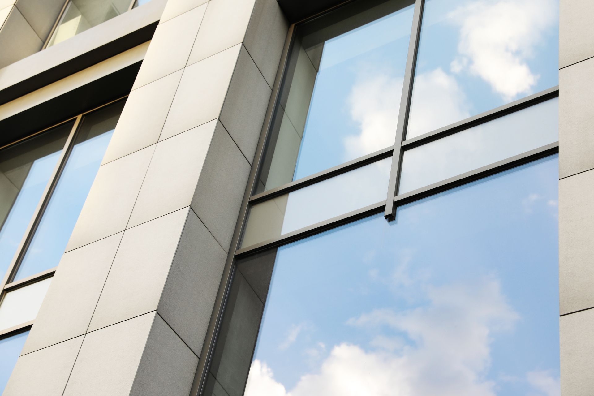 Modern glass building facade reflecting blue sky and clouds