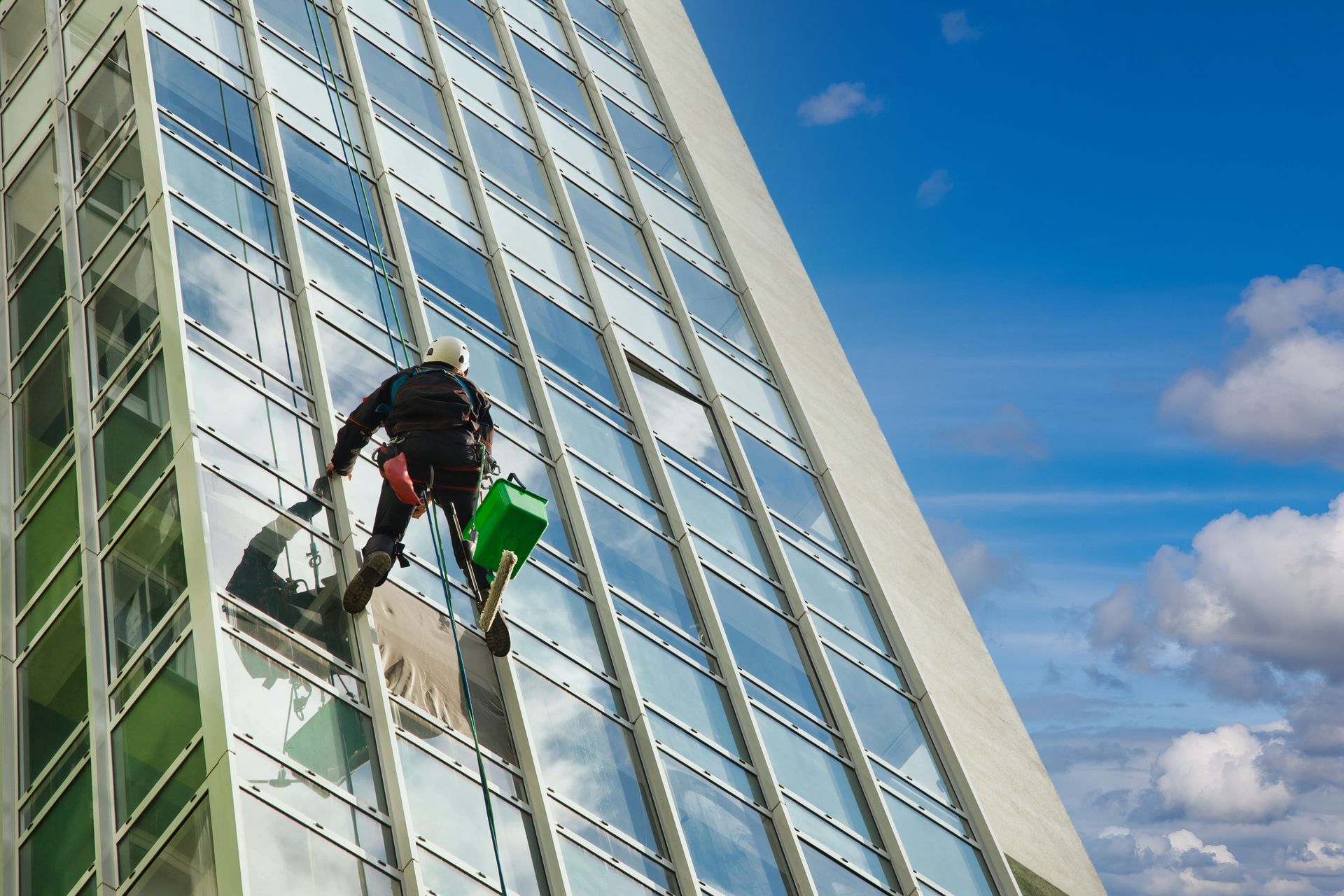 Window washer on ropes cleaning glass facade of a tall building against a blue sky