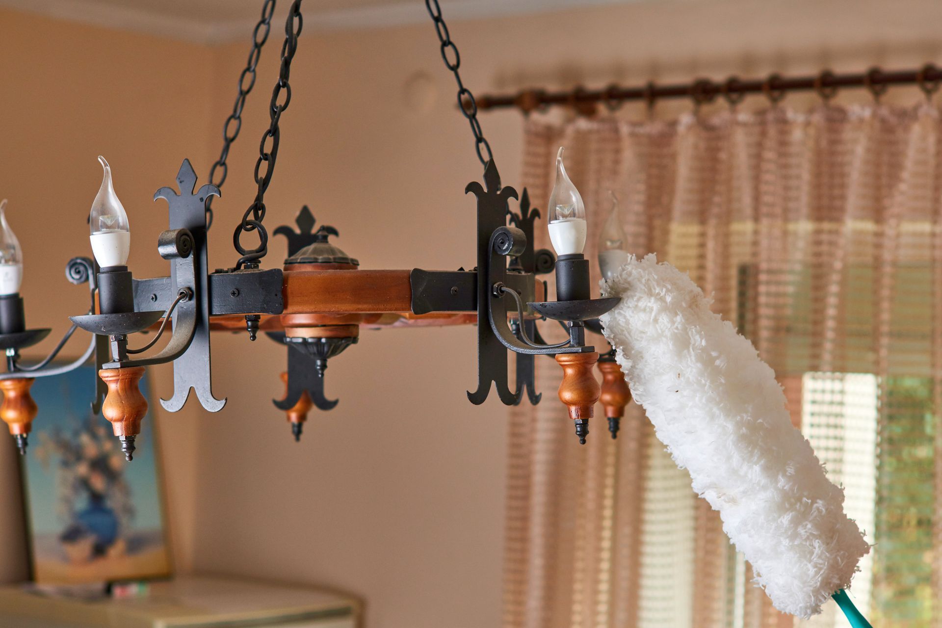 Chandelier being cleaned with a white cloth in a room by a window and curtains