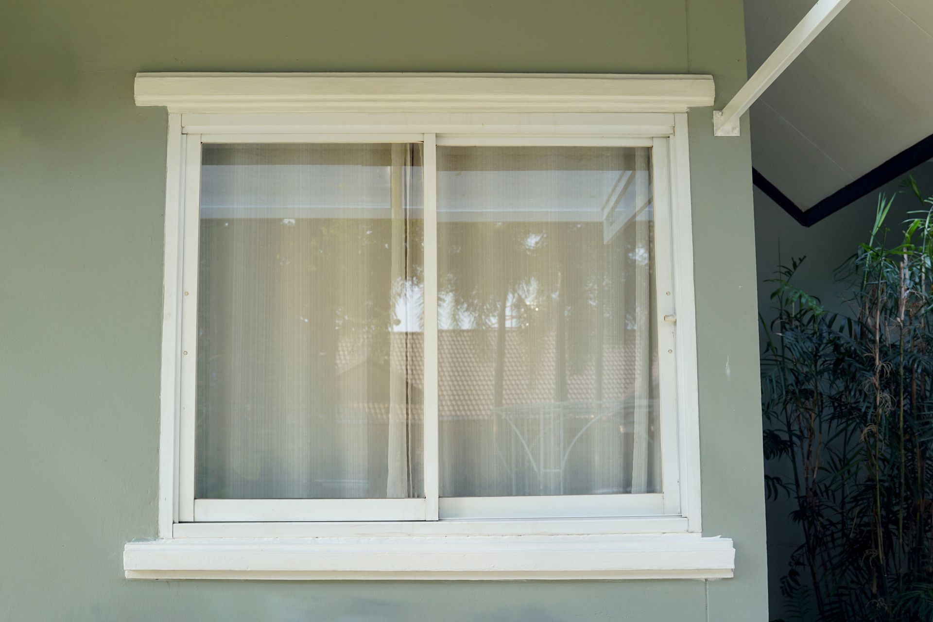 White sliding window with sheer curtains in a light green exterior wall