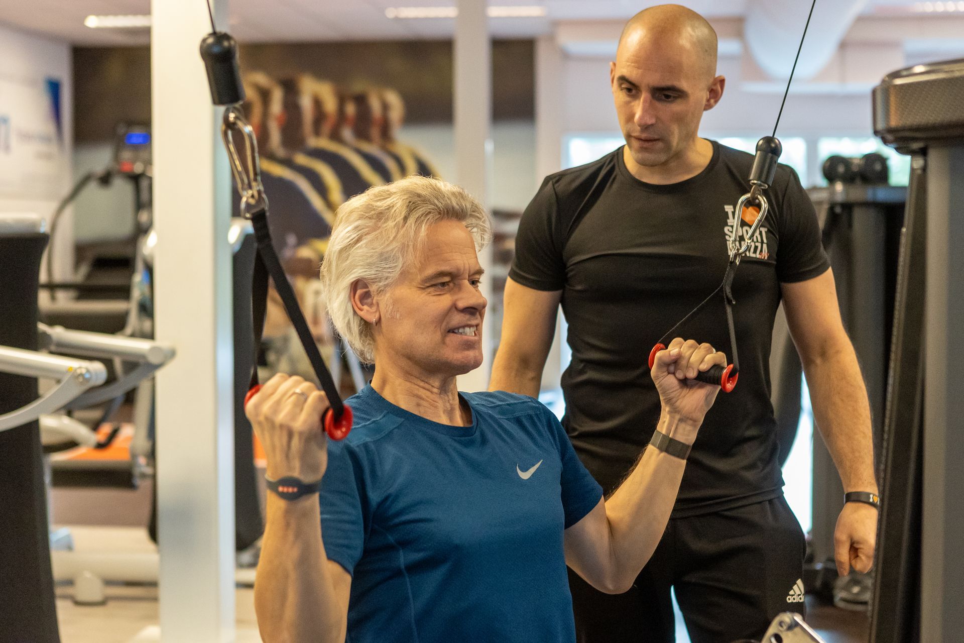 Een man leert een vrouw hoe ze een machine moet gebruiken in een sportschool.