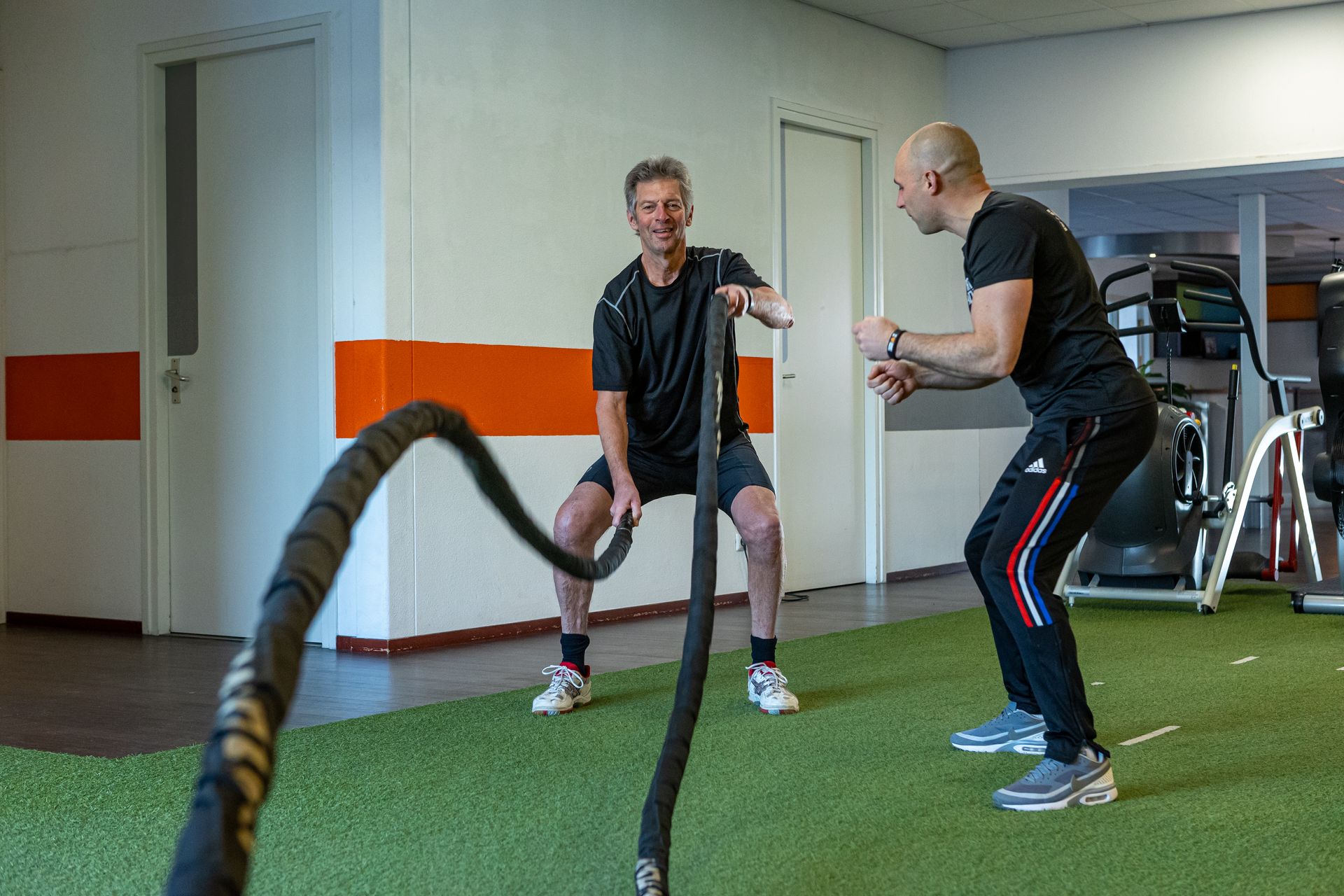 Twee mannen doen oefeningen met touwen in een sportschool.
