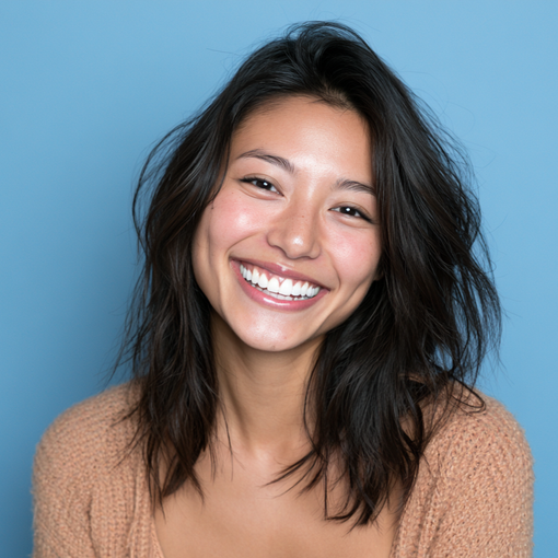 Smiling person with tousled dark hair against a blue background, wearing a tan sweater