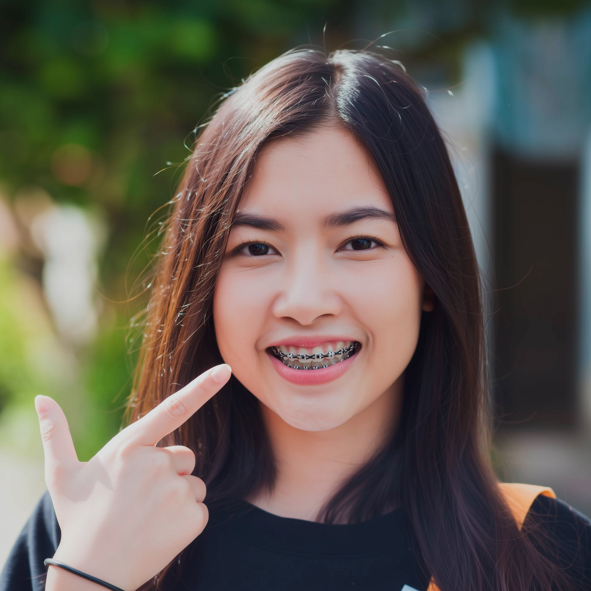 Smiling person pointing to metal braces while standing outdoors in daylight