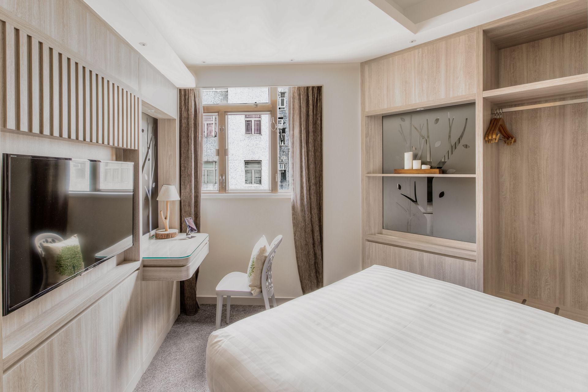 Bedroom with light wood paneling, TV, desk, bed, and window with curtains.