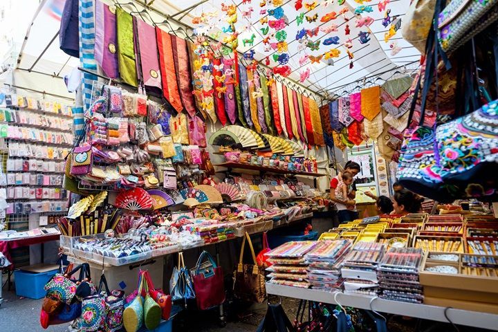 市场摊位上出售色彩缤纷的围巾、包包和小饰品。店主在柜台旁。